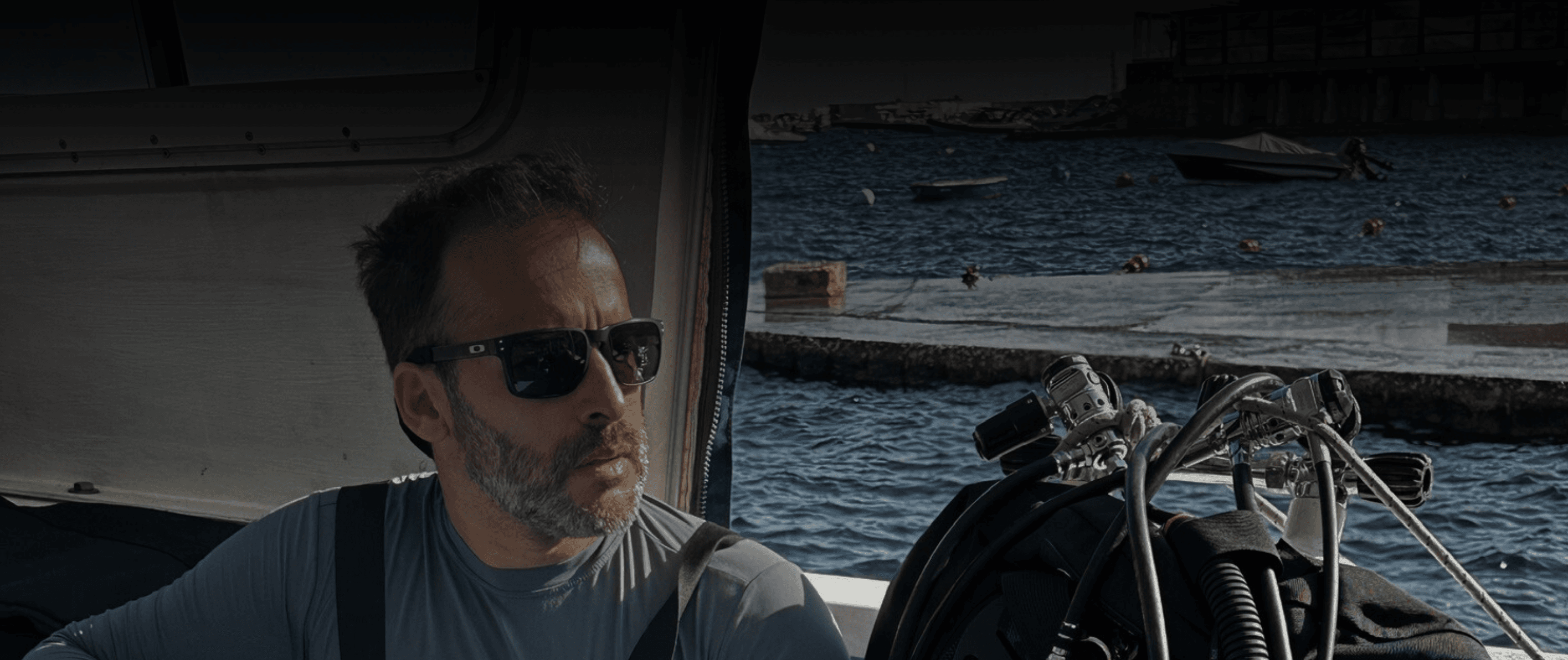 Valentim Magalhães de óculos escuros em um barco, com equipamento de mergulho ao lado